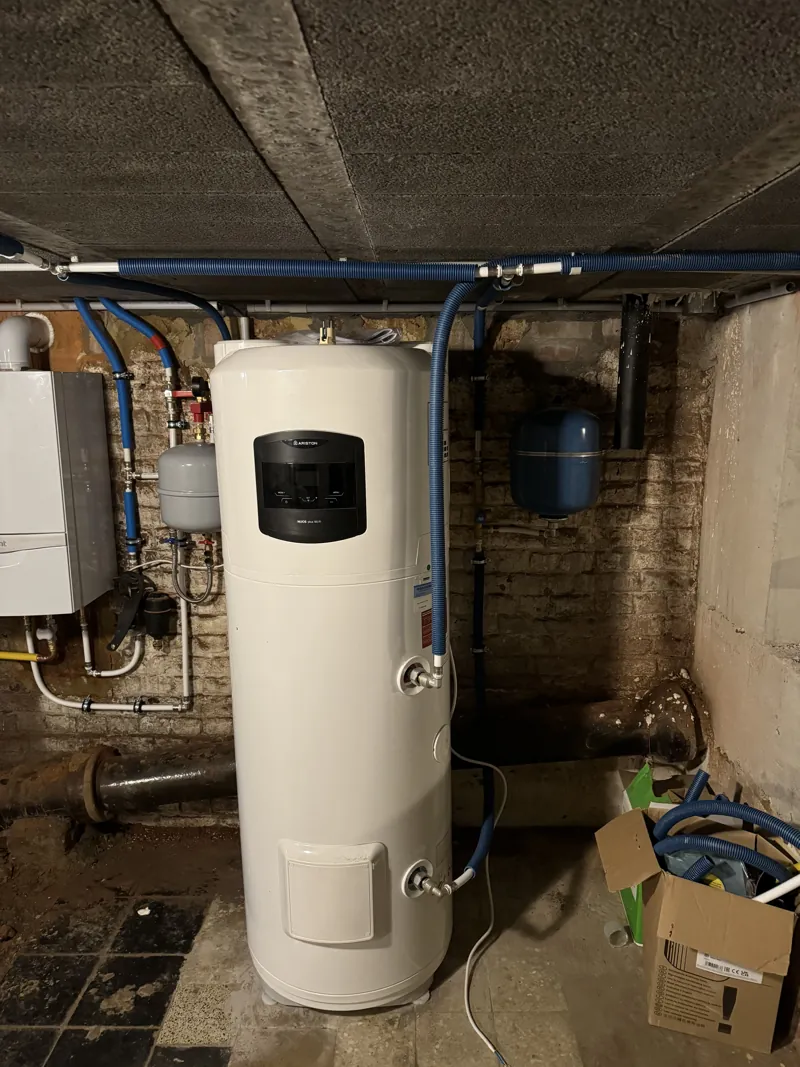 Chauffe-eau thermodynamique Ariston Nuos Plus installé à côté d'une chaudière Vaillant dans une cave en brique