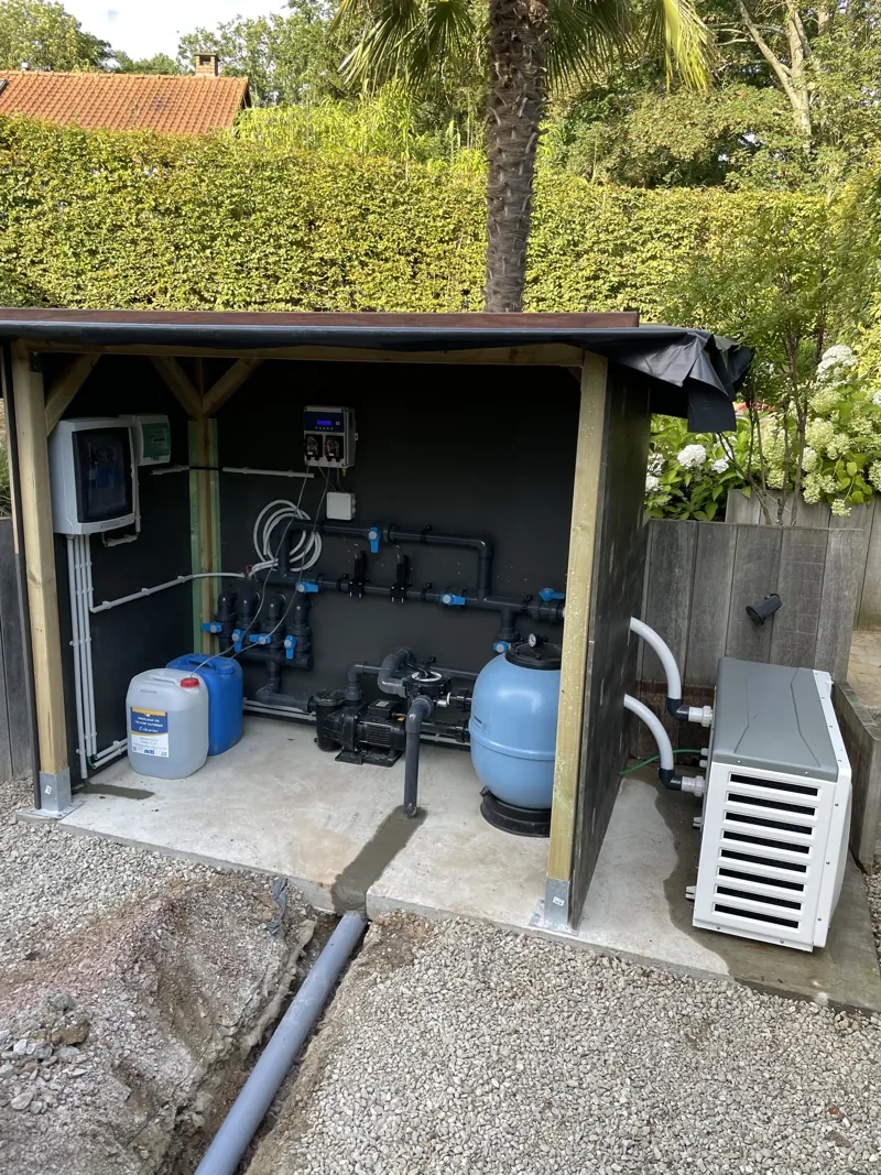 Abri technique de piscine ouvert vu de l'extérieur dans un jardin, avec filtre, pompe et pompe à chaleur de piscine
