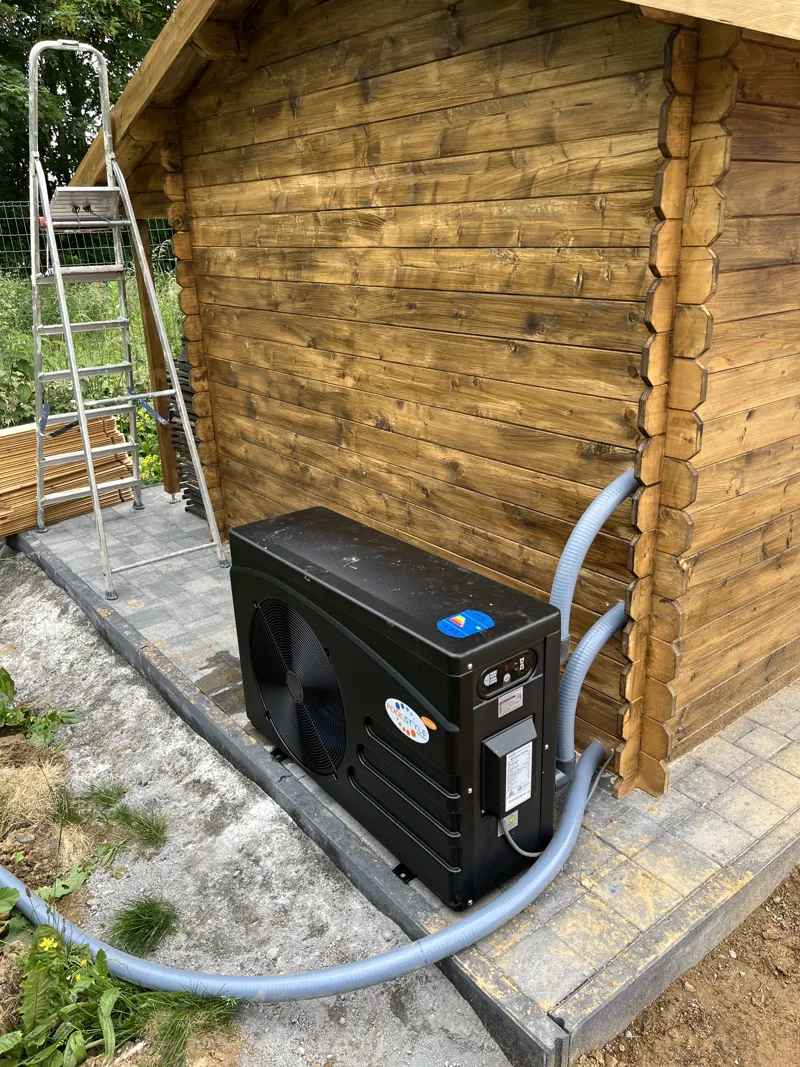Pompe à chaleur de piscine noire installée contre un chalet en bois