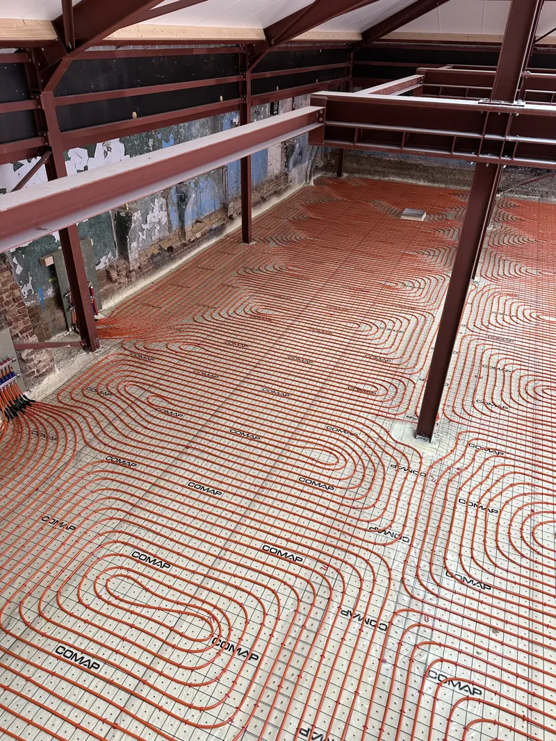 Boucles d'un grand plancher chauffant posées dans un hall à charpente métallique rouge