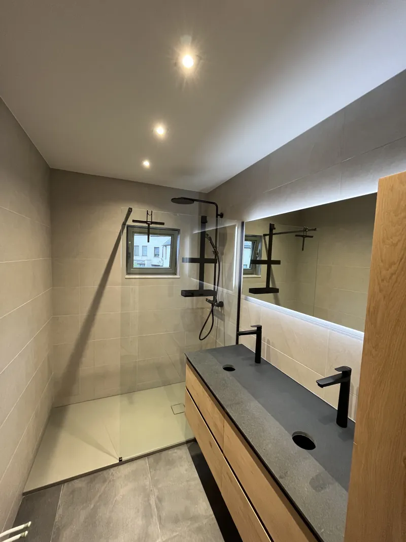 Meuble double vasque en bois et douche dans une salle de bain terminée au carrelage gris