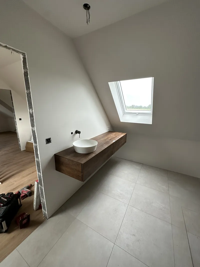 Vasque posée sur un plan en bois sous une fenêtre de toit, salle de bain au carrelage gris